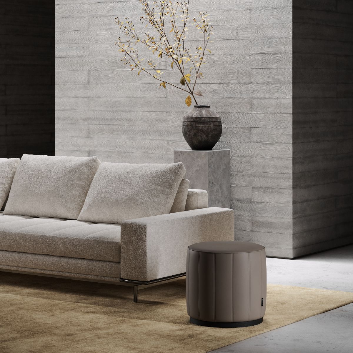 upholstered poufs selection (5) A modern living room with a beige sofa and a brown cylindrical pouf on a beige rug. A minimalist vase with branches sits on a concrete pedestal, creating a serene atmosphere.