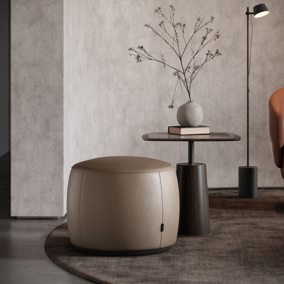 upholstered poufs selection (6) A modern living room with a beige pouf, a small round table holding a vase with twigs, a book, and a dim floor lamp, exudes a minimalist, calm vibe.