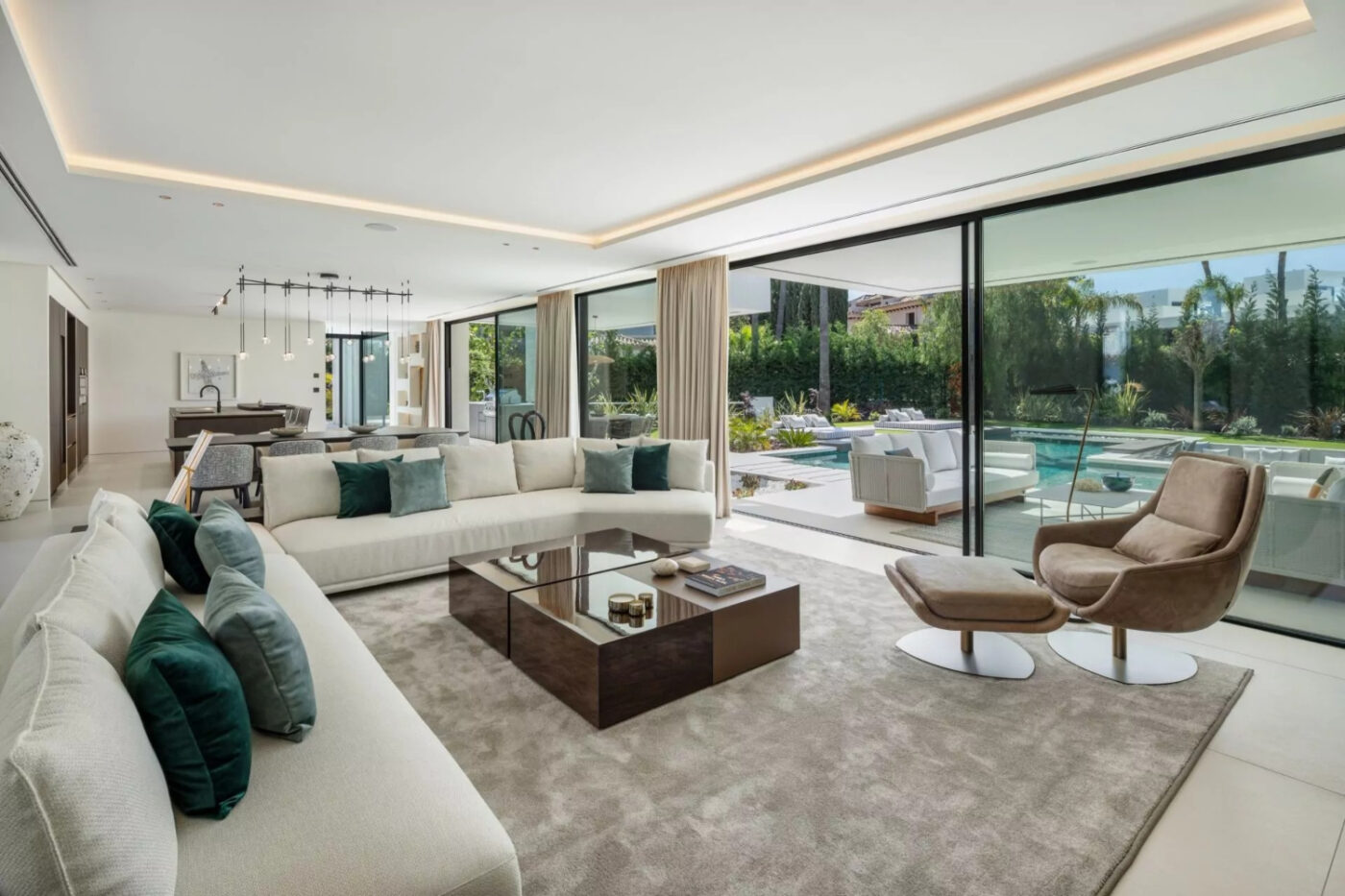 Spacious modern living room with expansive windows, showcasing a view of a serene pool outside. By Blanca Pera with Elba Armchair in brown velvet.
