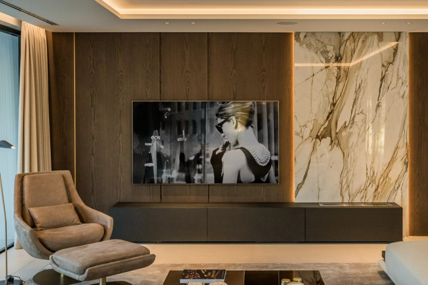 Contemporary living room with elegant marble walls and a spacious television setup. By Blanca Pera with Elba Armchair in velvet brown.