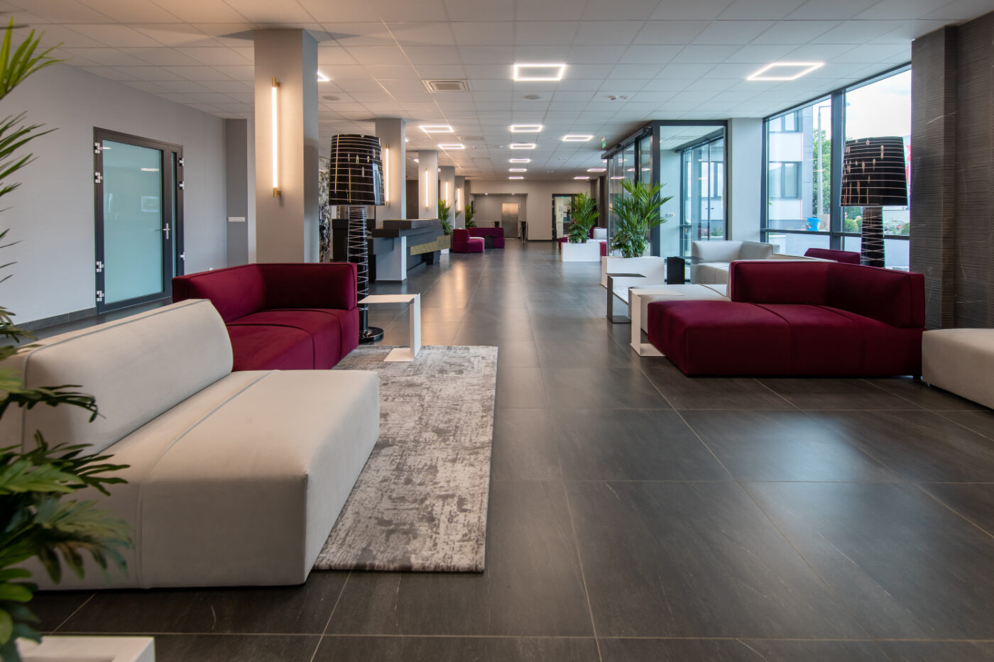 A spacious lobby featuring a large modular sofa in burgundy and beige, creating a welcoming atmosphere. Commercial interior design.